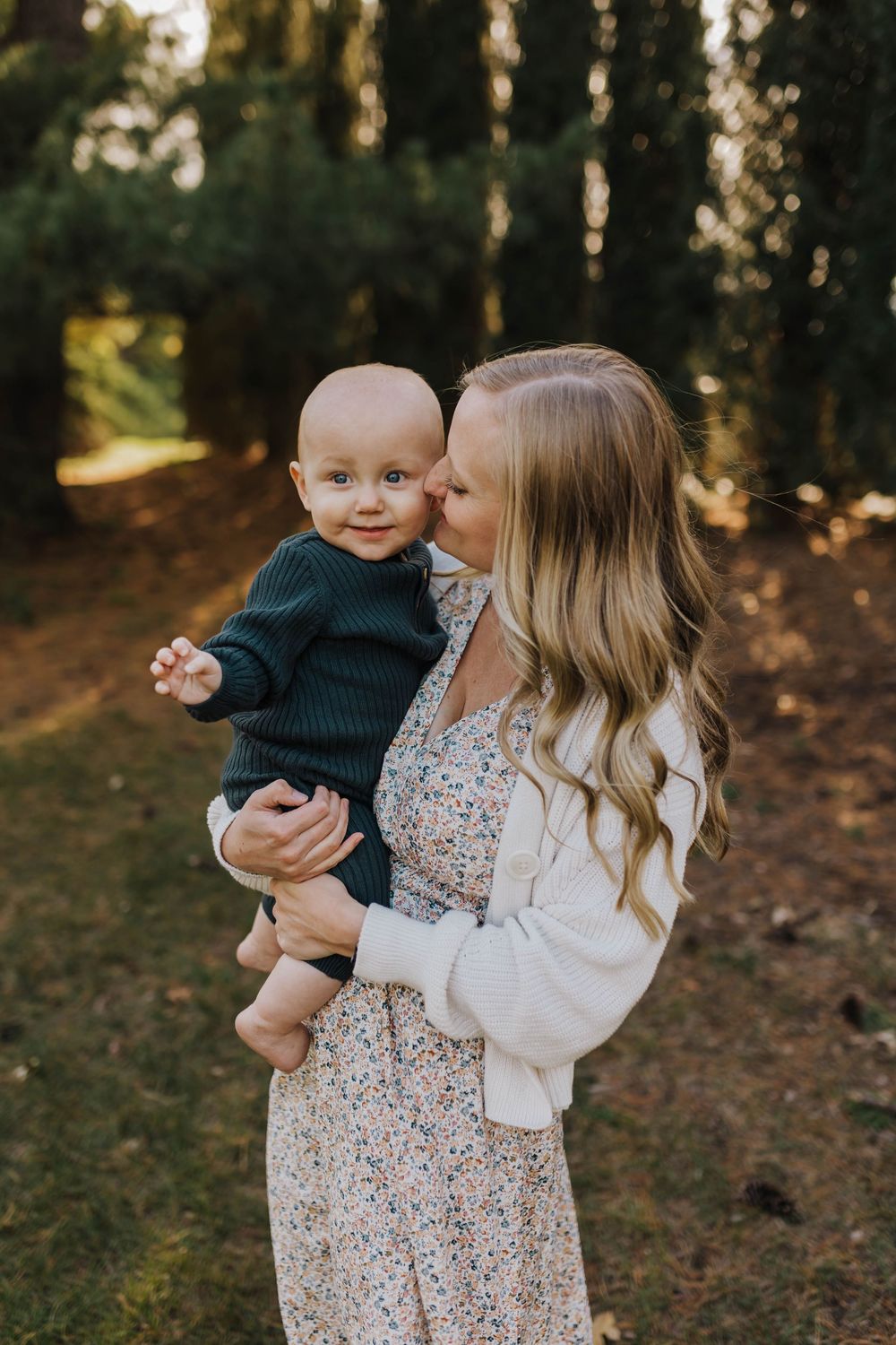 A tender moment captured outdoors in a wooded setting with natural sunlight filtering through the trees.