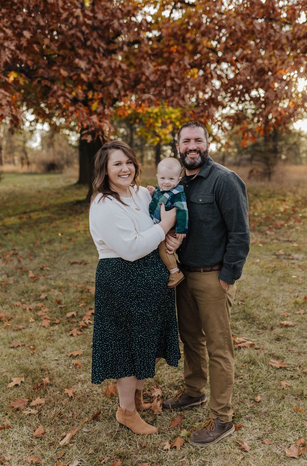 Family enjoying a warm autumn day together outdoors with fallen leaves and brown foliage in the background.