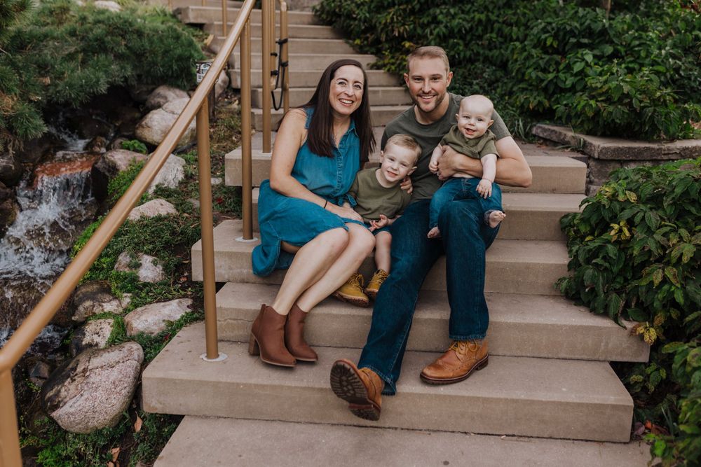 A family sits together on outdoor stone steps next to a garden.