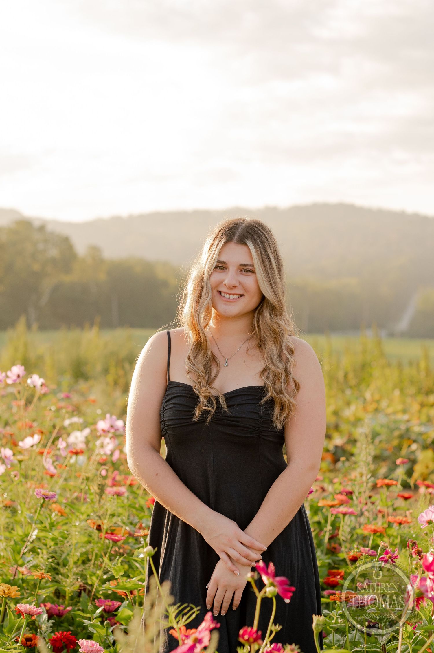 A beautiful outdoor portrait in a vibrant wildflower field at golden hour with rolling hills in the background.