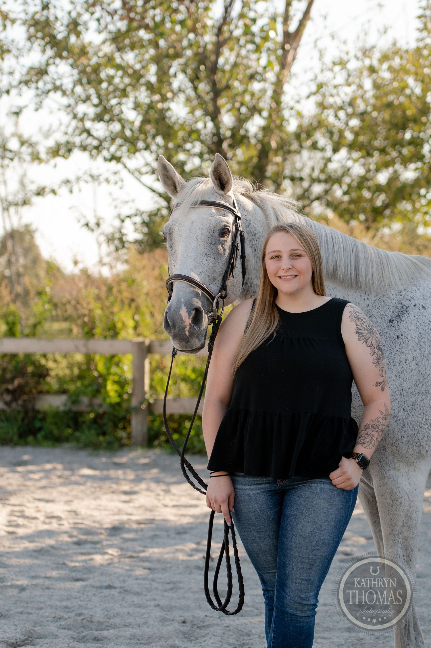 A casual equestrian portrait with a grey horse in a rustic outdoor setting.