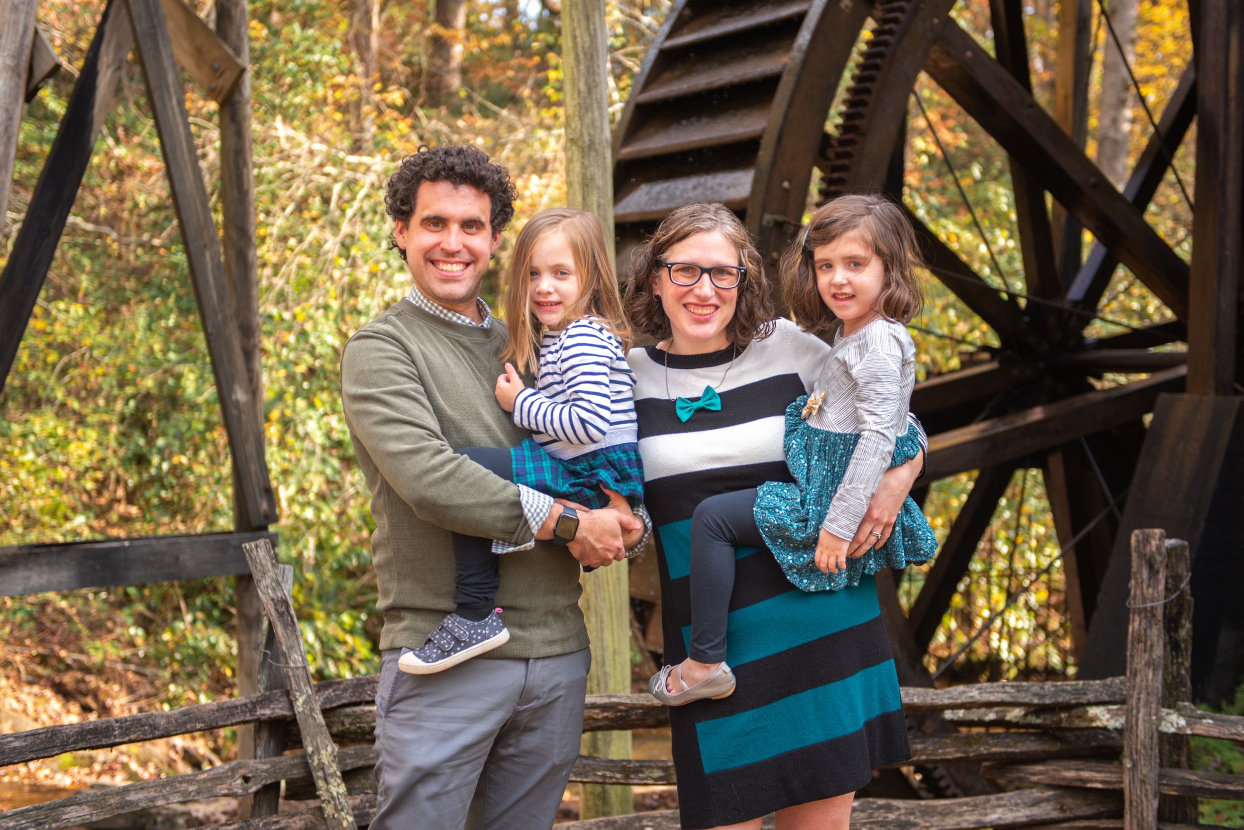 A happy family poses together on an old wooden bridge structure during fall.