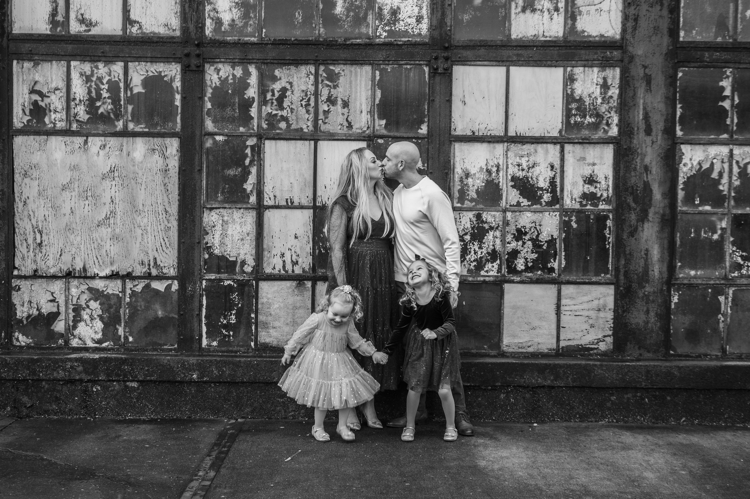 A black and white photo of a small child and two adults standing against an industrial window wall.