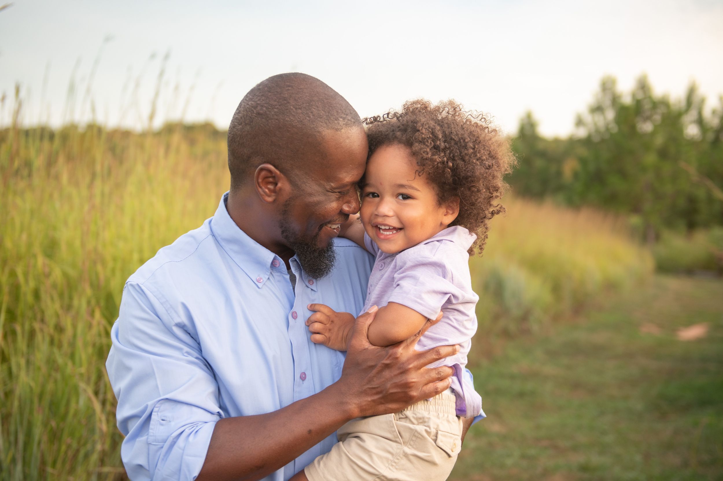 A tender moment shared outdoors in a sunlit field with tall grass.