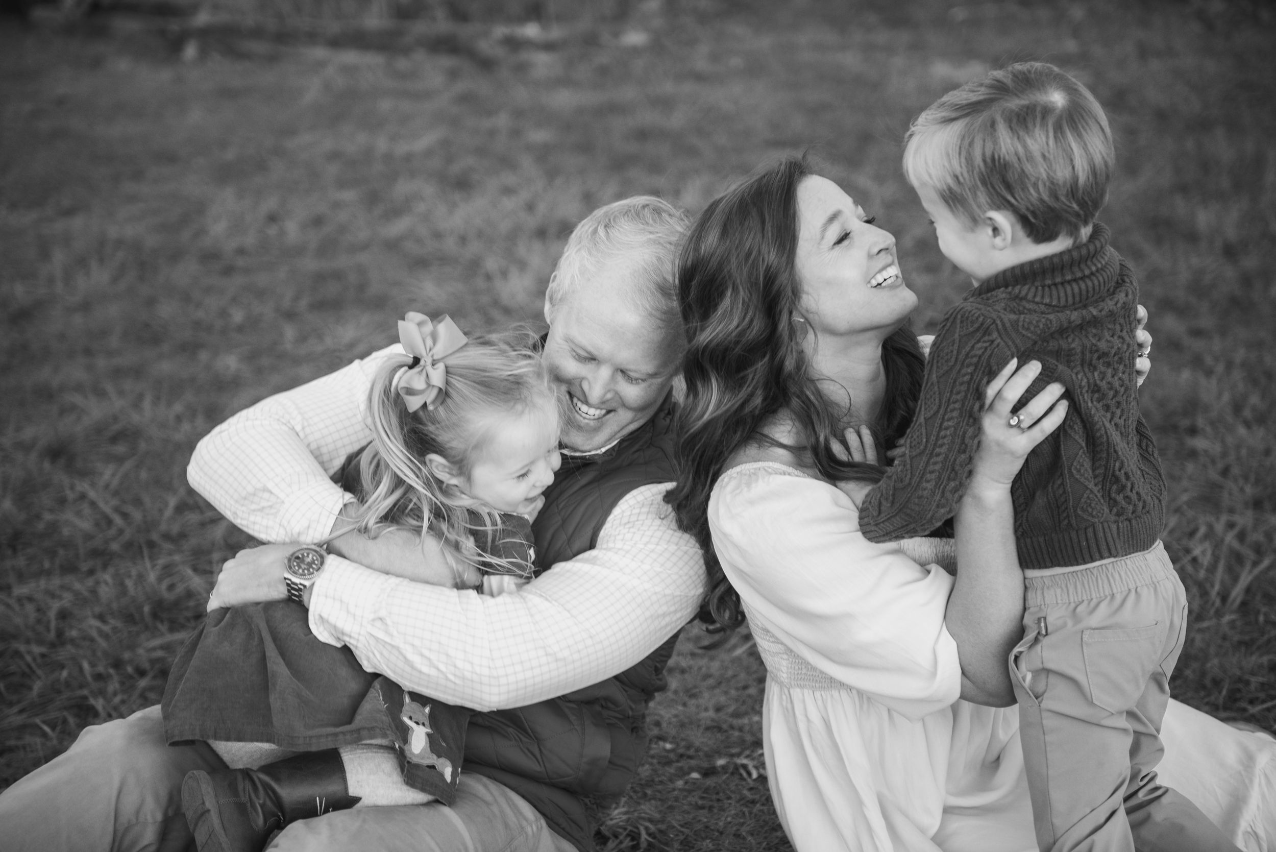 A candid family moment captured in black and white showing embrace and laughter outdoors.