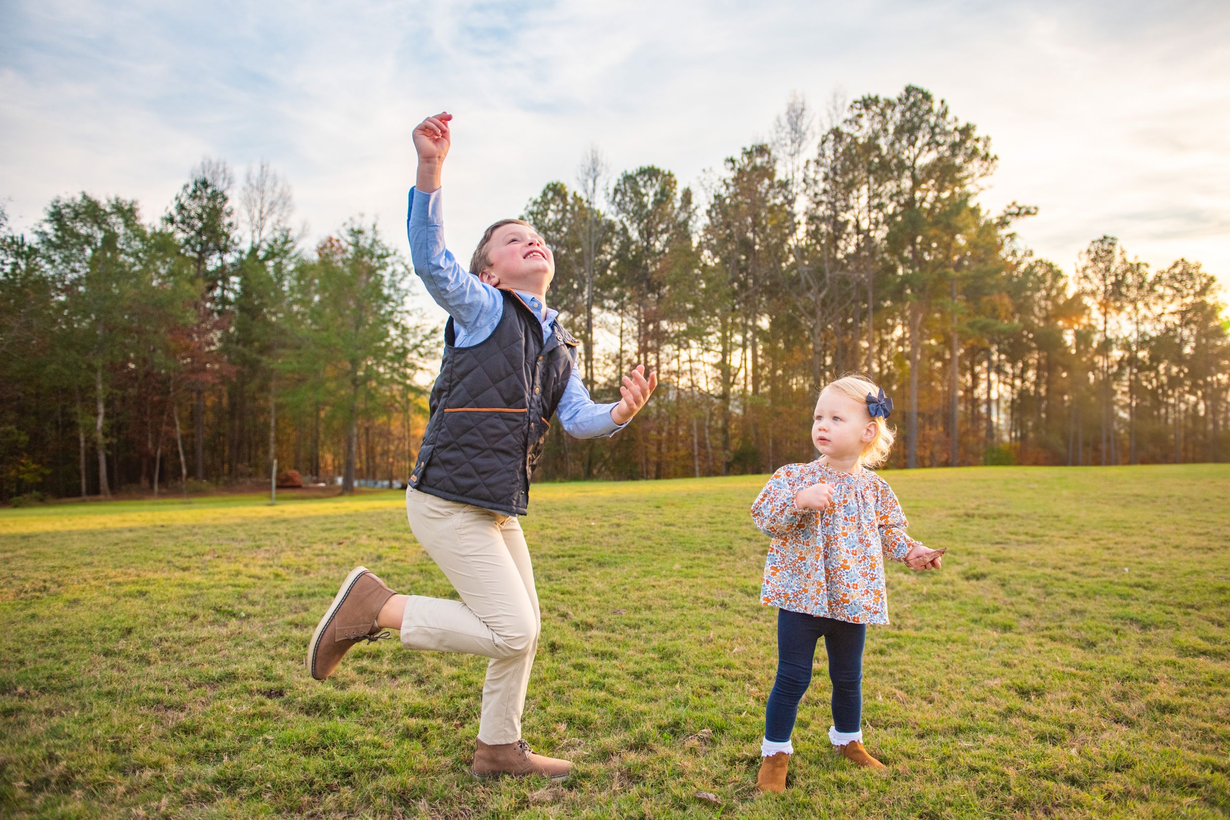 Two people play and jump together in a grassy field during sunset.