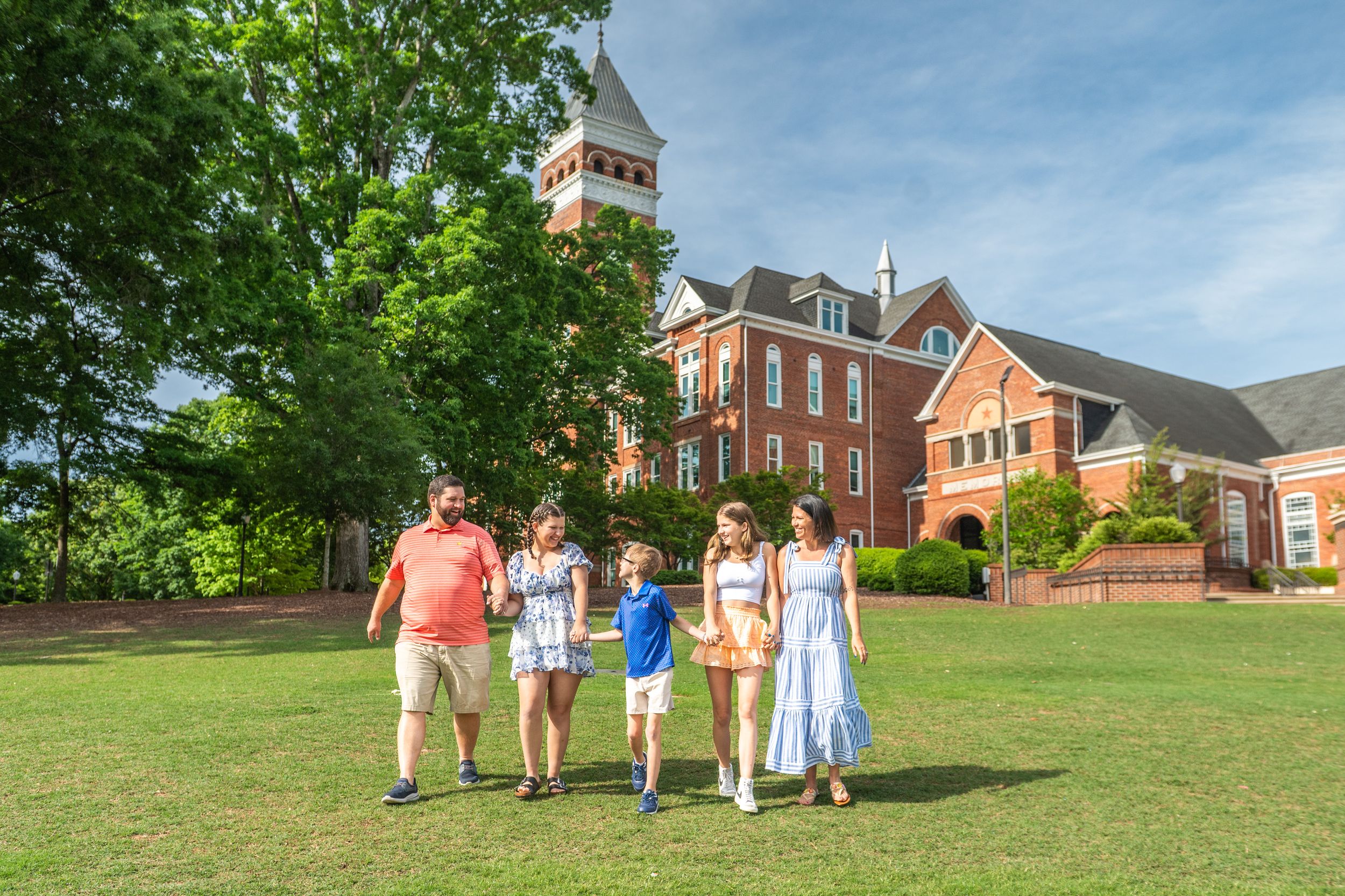 A group walks across a lawn with traditional red brick college buildings in the background.
