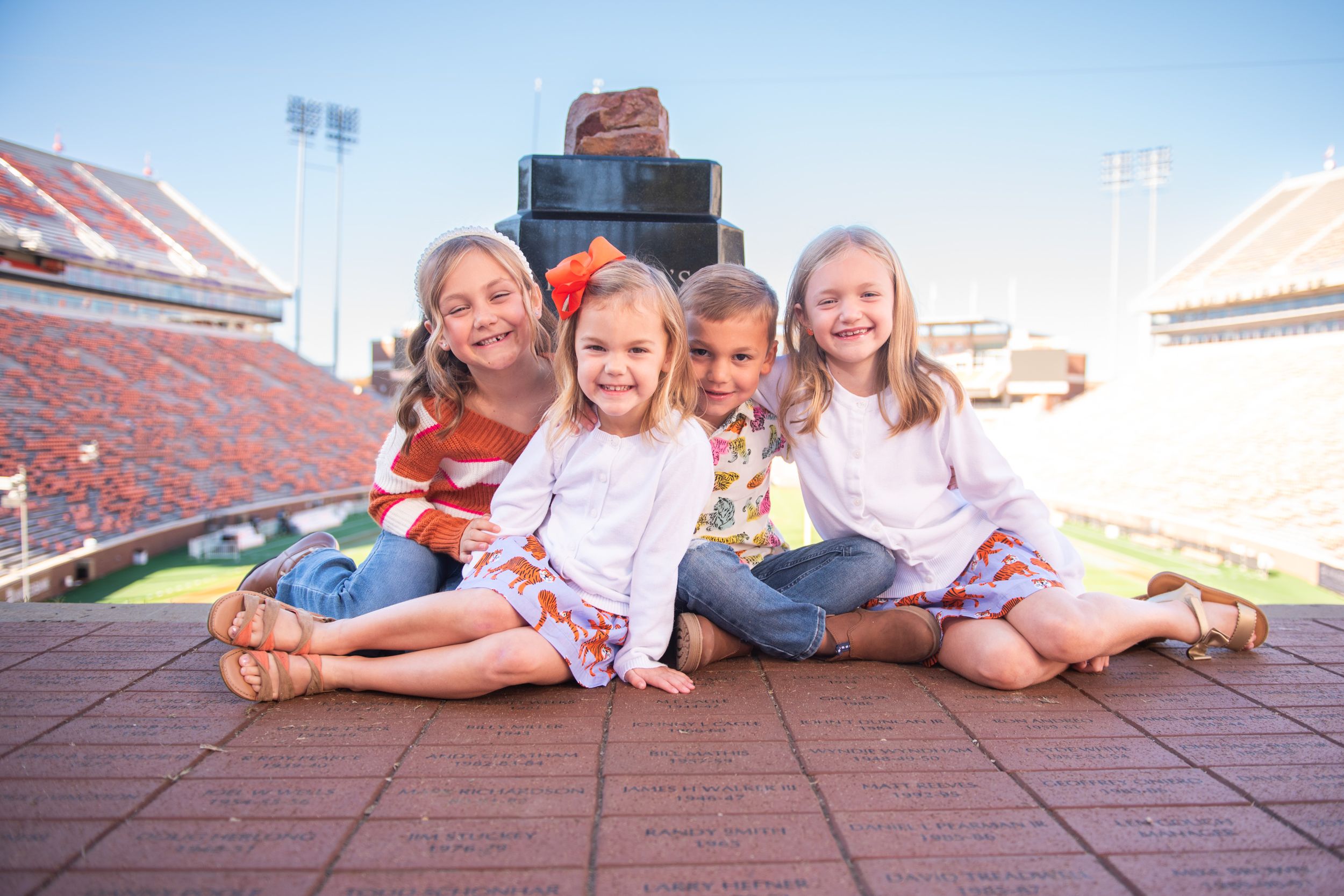 Young children sit together smiling in a large football stadium with red seats.