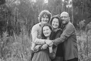 A candid outdoor family portrait showing four people embracing and laughing together in a field.
