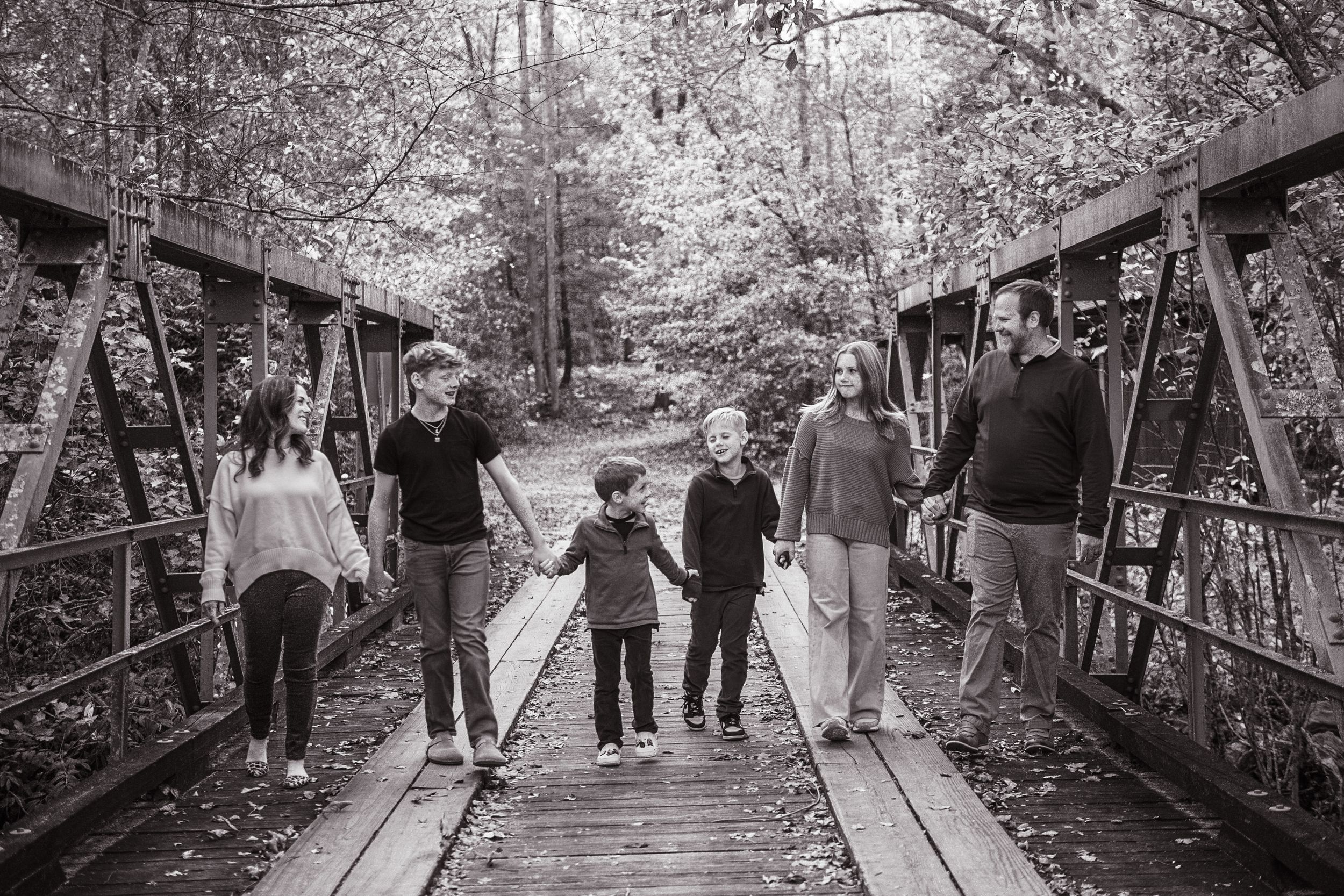 A group walks together on a rustic wooden bridge surrounded by autumn trees.
