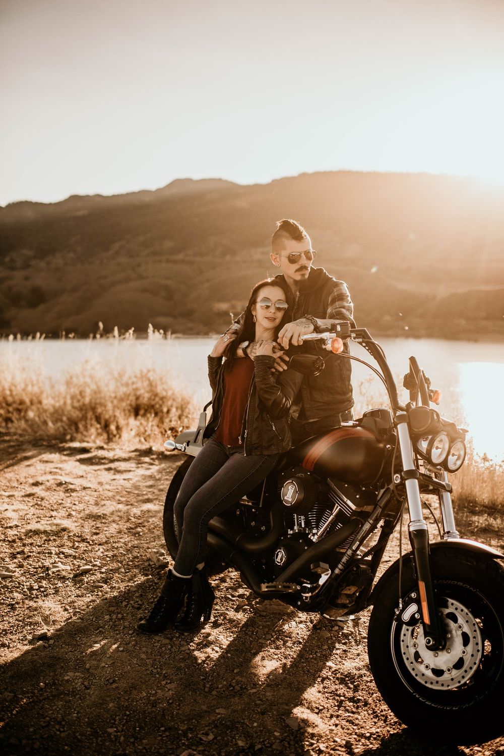 Couple on motorcycle against sunset backdrop in mountain landscape.