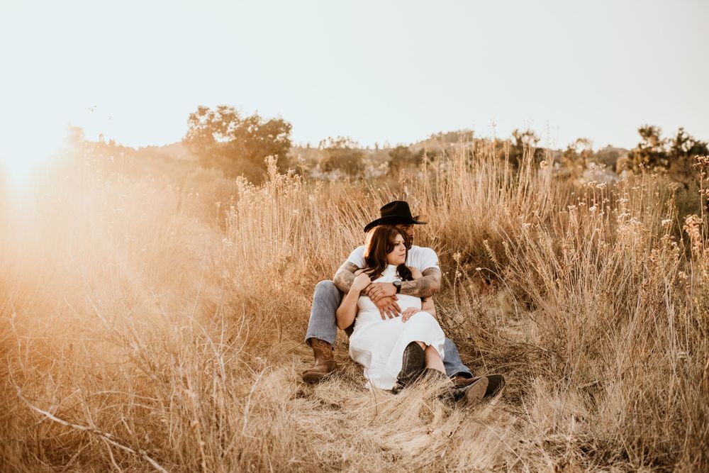 Couple sitting in tall golden grass during sunset in rustic setting.