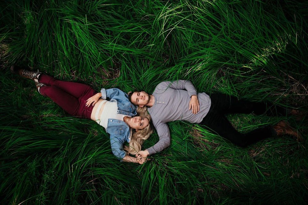 Two people lie in tall green grass during an intimate outdoor photo session.