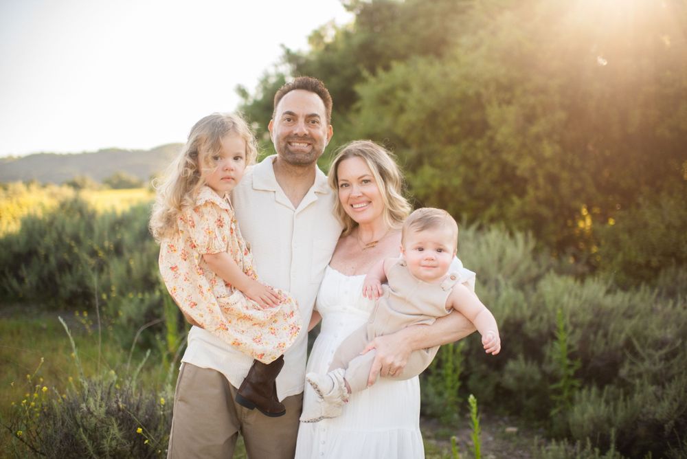 A family poses together in an outdoor setting at sunset with golden light filtering through trees in the background.
