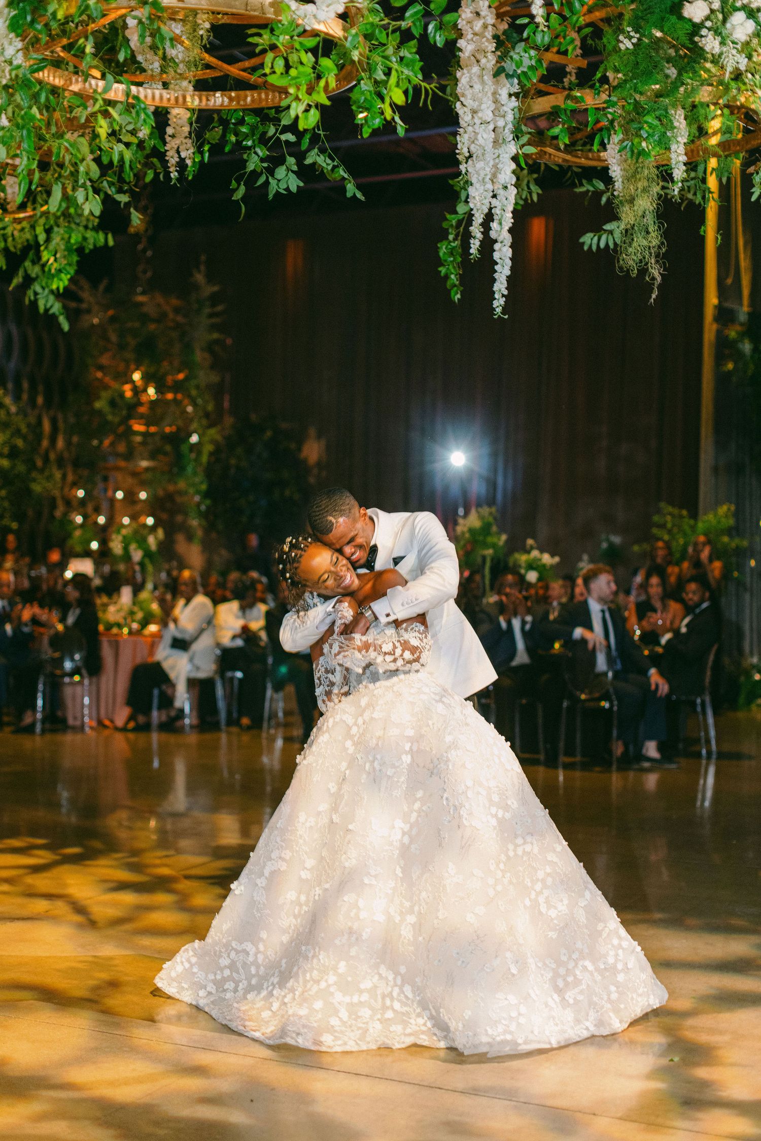 A couple sharing their first dance under hanging floral decorations at their wedding reception.