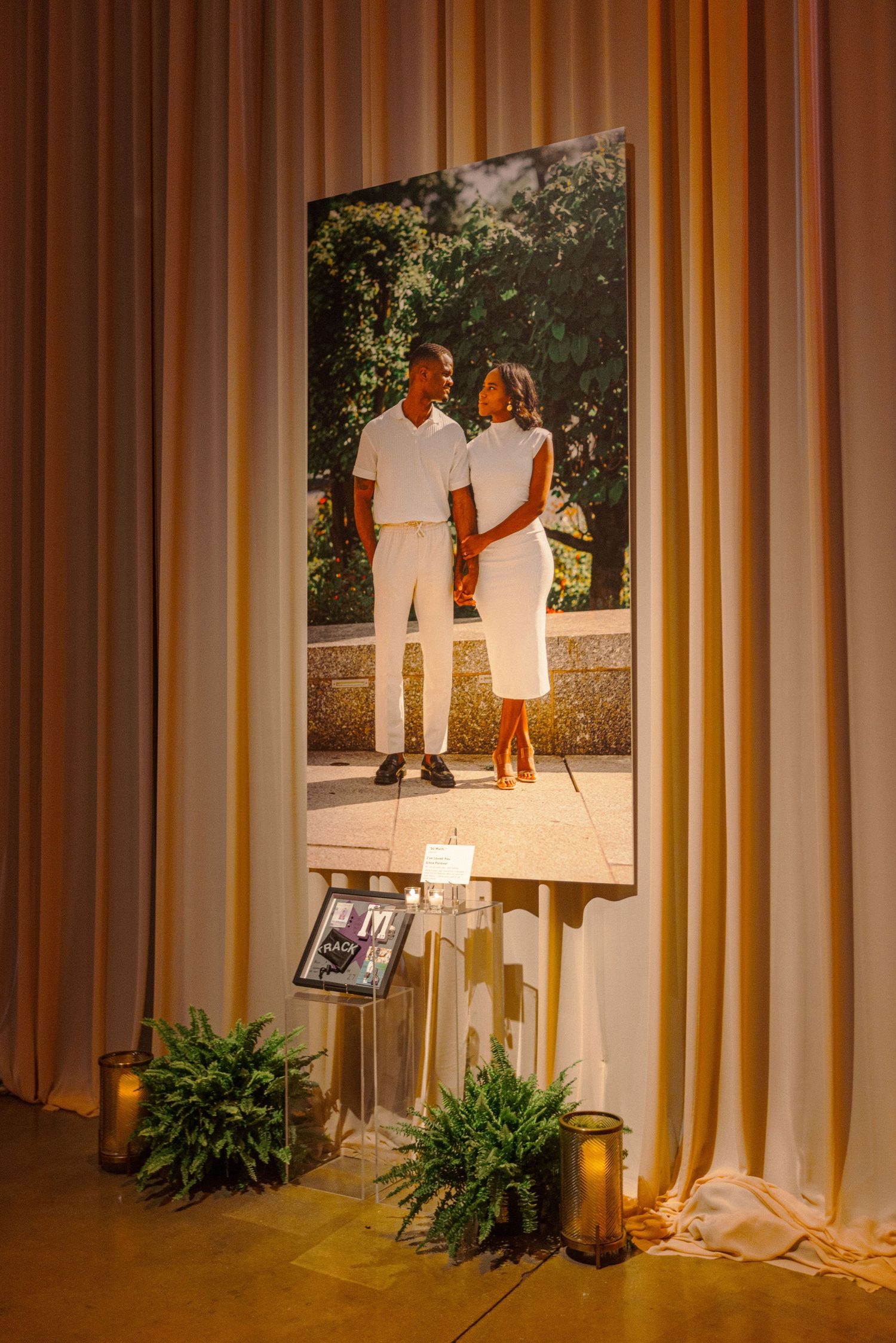 Large portrait display with romantic lighting and decorative plants at wedding venue.
