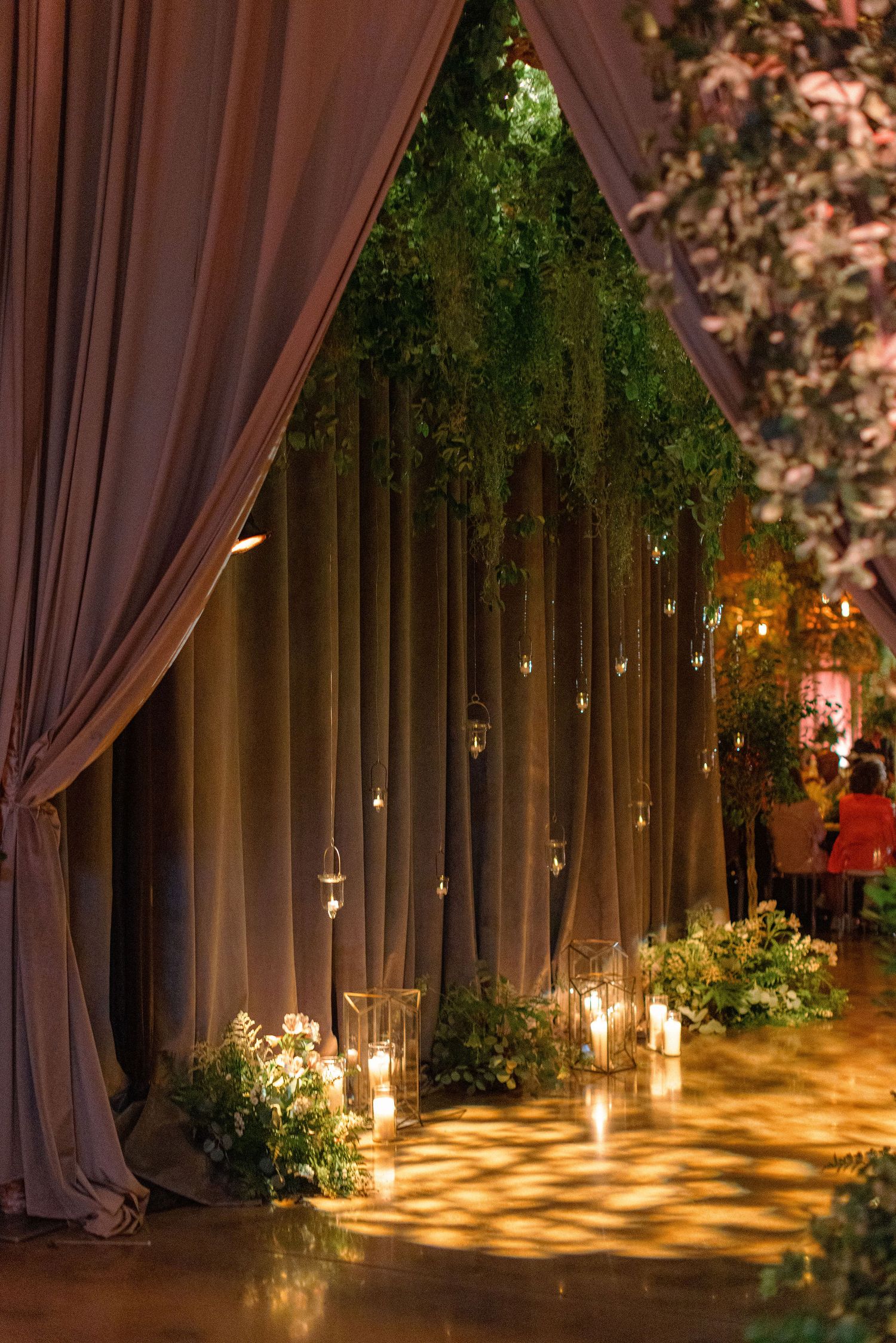 Romantic wedding venue decor with hanging greenery, draped curtains, and candlelight.