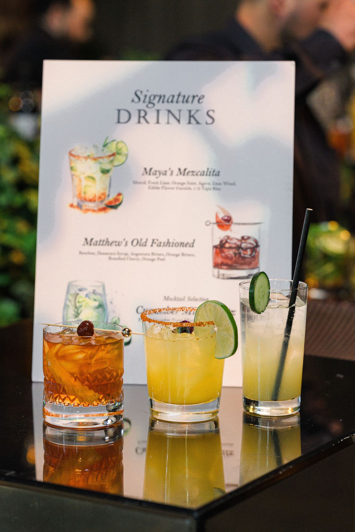 Signature cocktail menu displayed with three garnished drinks on a reflective surface.