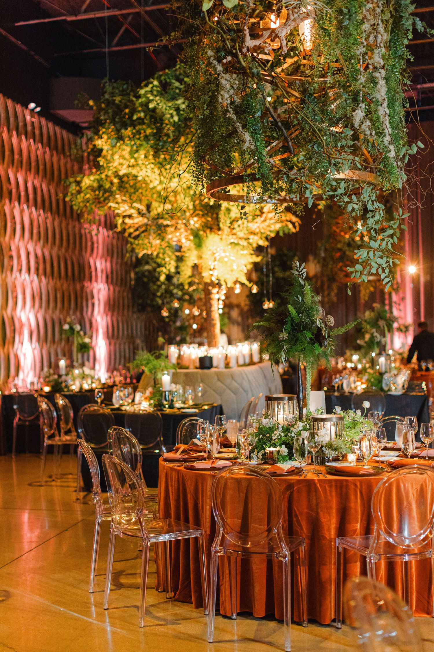 Elegant wedding reception venue with hanging greenery and amber lighting over rustic tables.