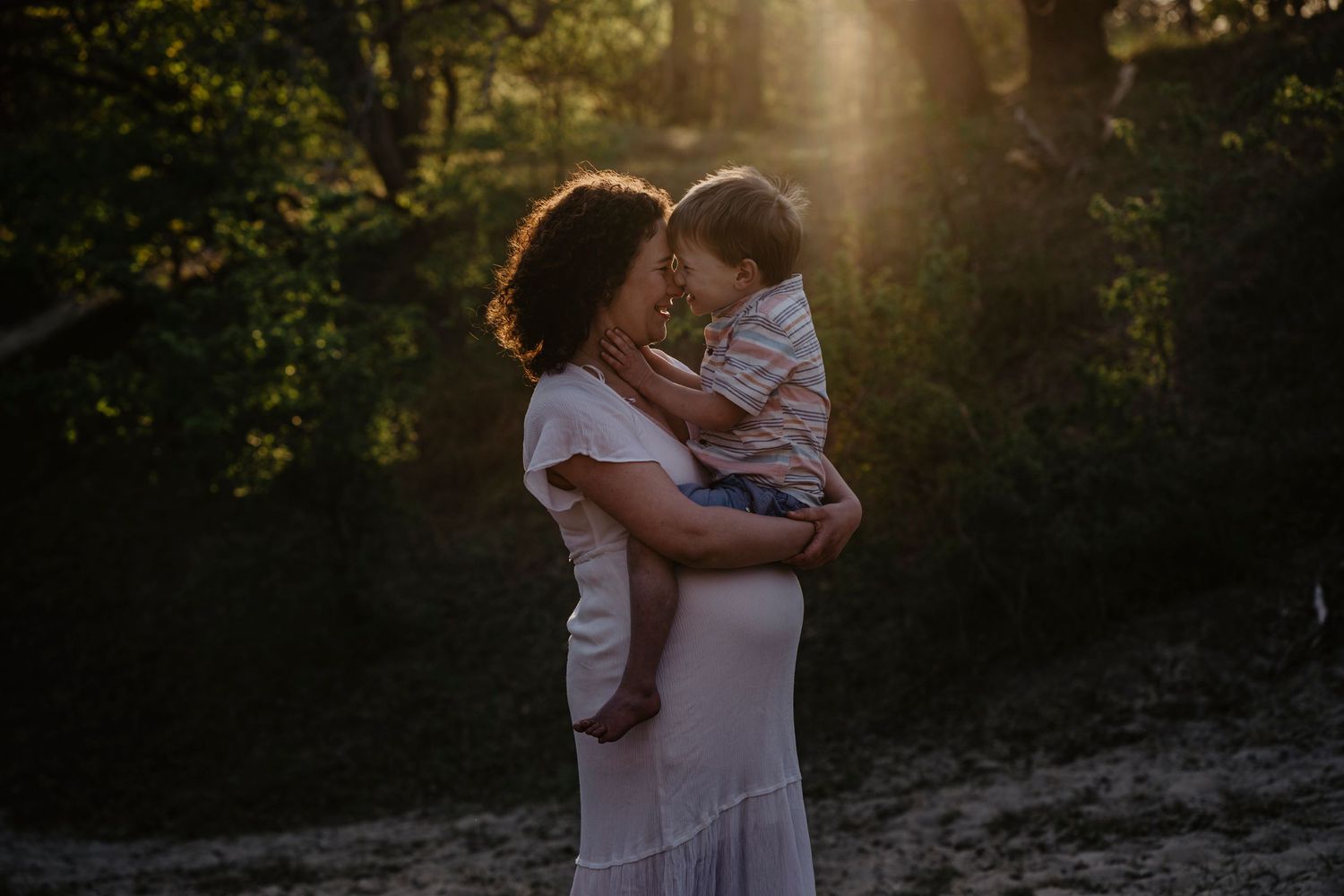Mãe abraça o filho em meio à natureza, numa sessão fotográfica familiar cheia de luz natural, afeto e conexão autêntica.