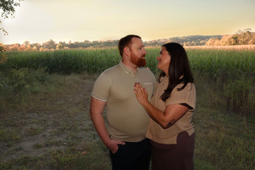 Couple gazing at each other at golden hour in front of a green cornfield at sunset.