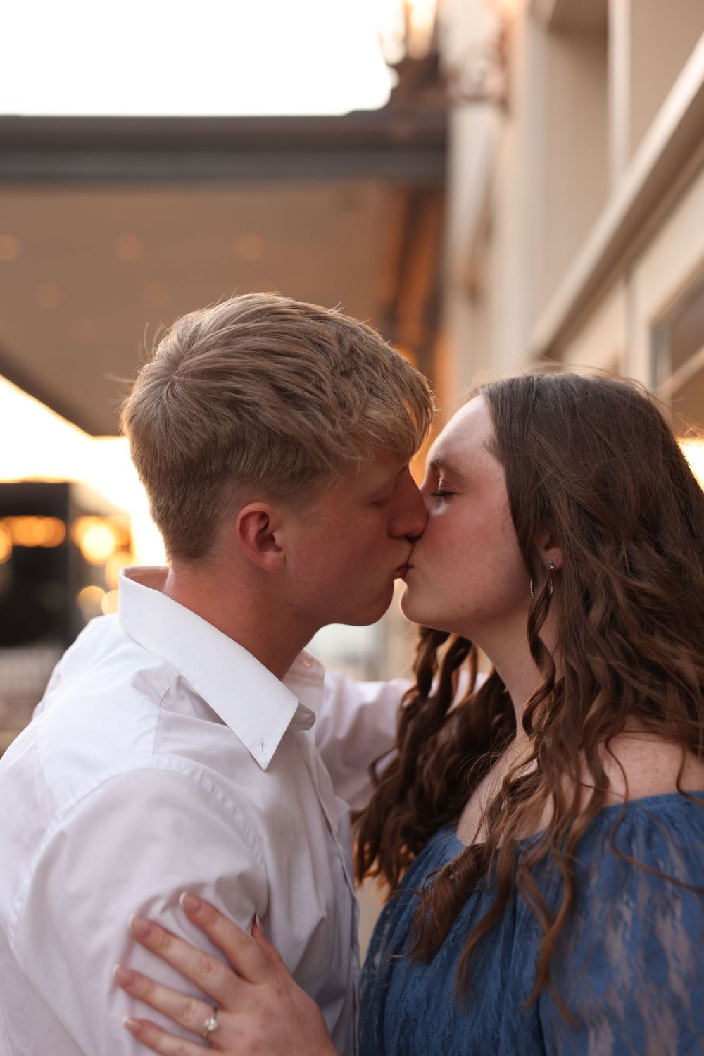 Young couple sharing a tender kiss outdoors during golden hour at a train station setting.