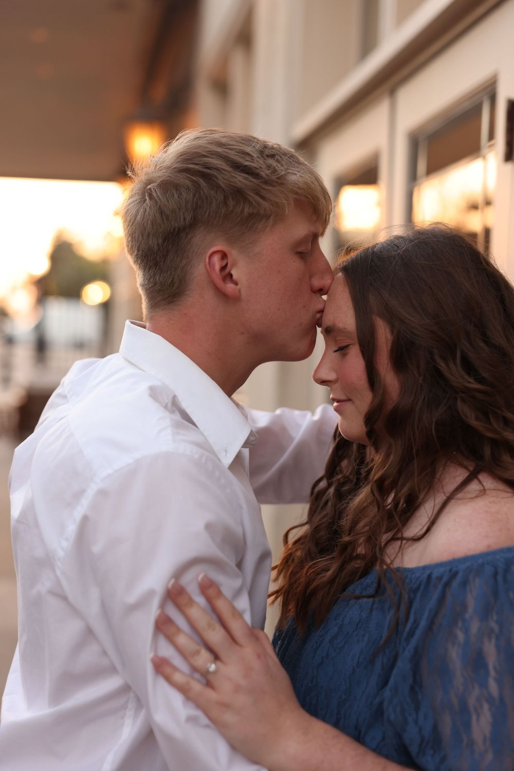 Young couple in a romantic embrace, man kissing woman's forehead during a warm sunset session.