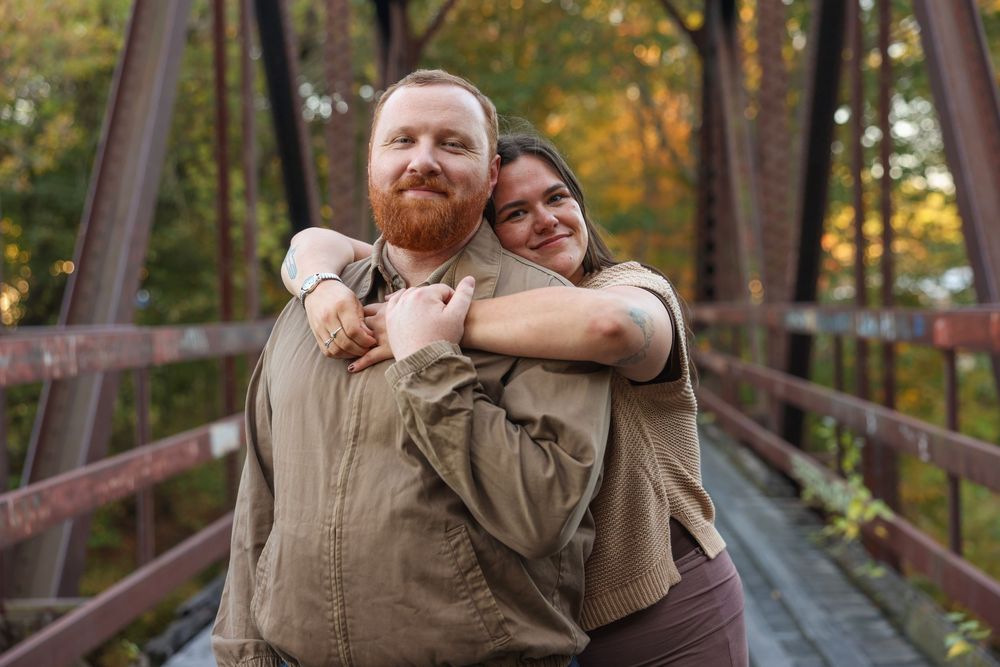 Happy couple embracing on a rustic iron bridge surrounded by colorful autumn foliage.