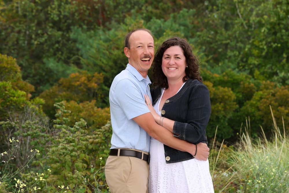 Smiling couple embracing outdoors surrounded by lush green foliage.