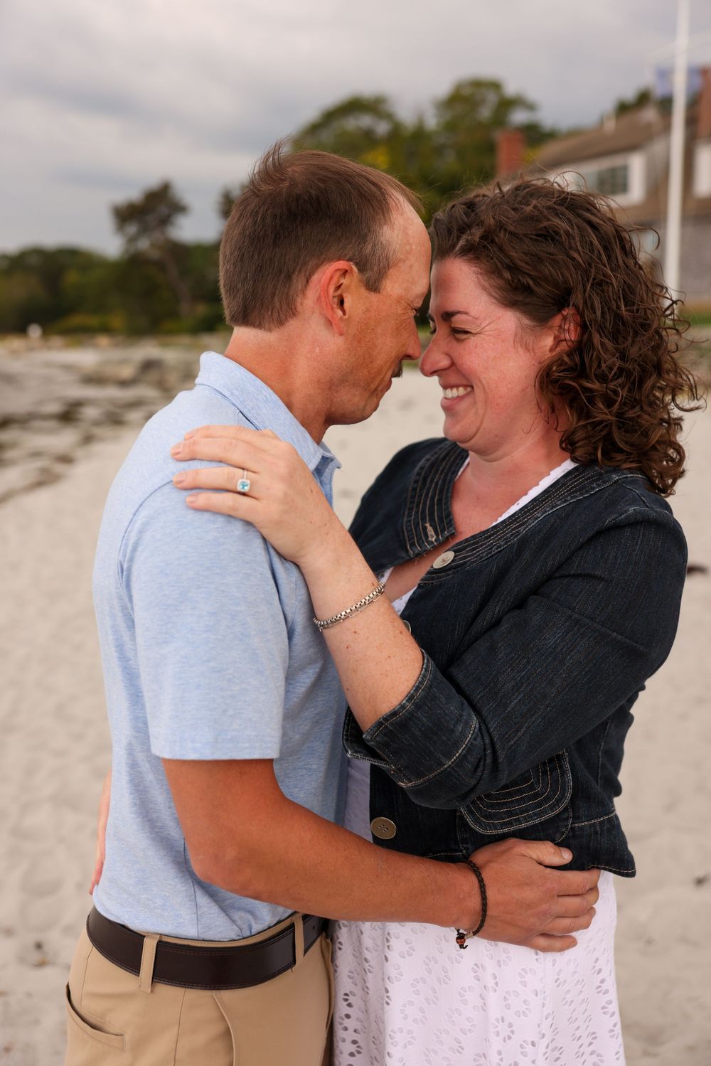 Couple touching foreheads and smiling on a sandy beach.