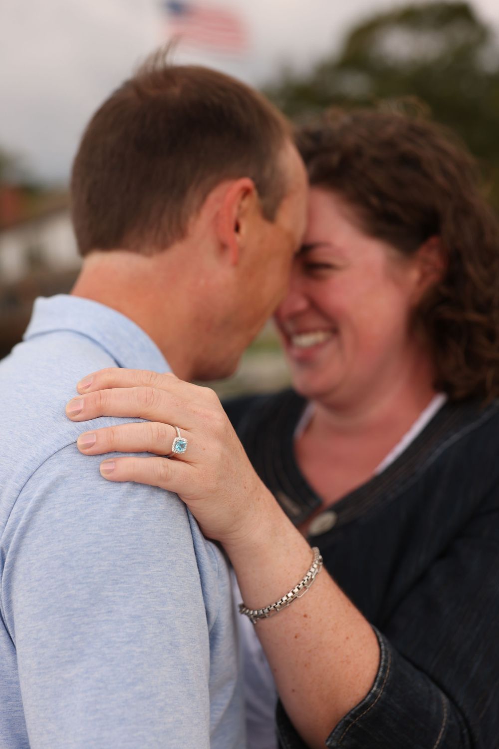 Close-up of woman with engagement ring embracing man on beach.