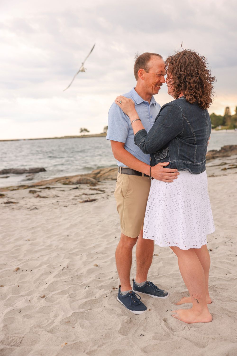 Couple embracing on a sandy beach at sunset near the ocean.