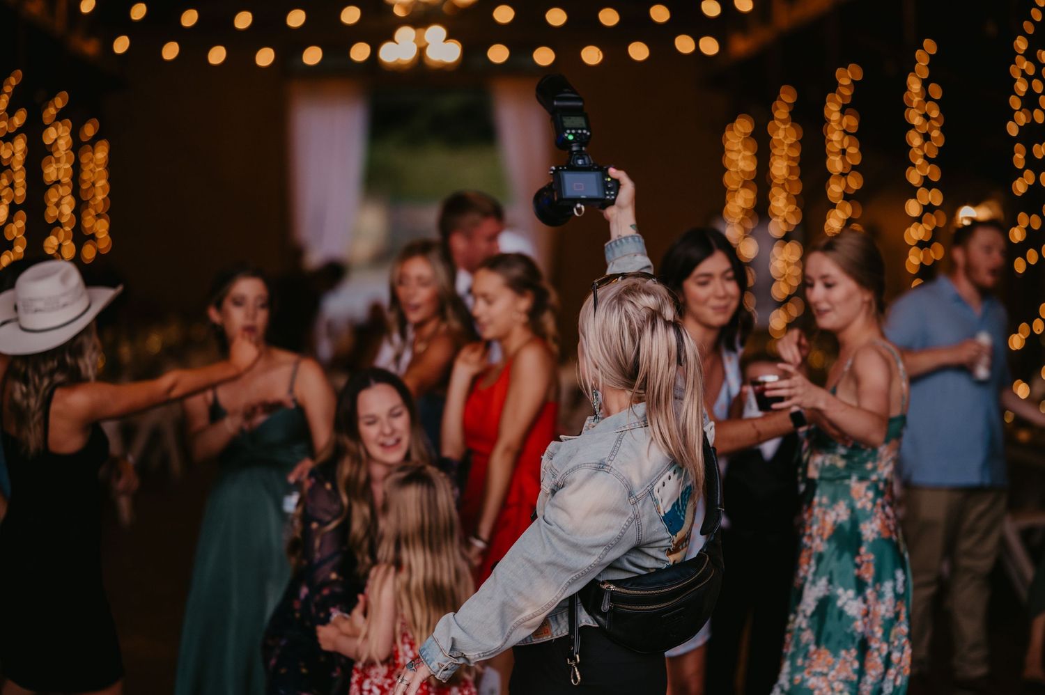 People dancing and celebrating at nighttime event under string lights.