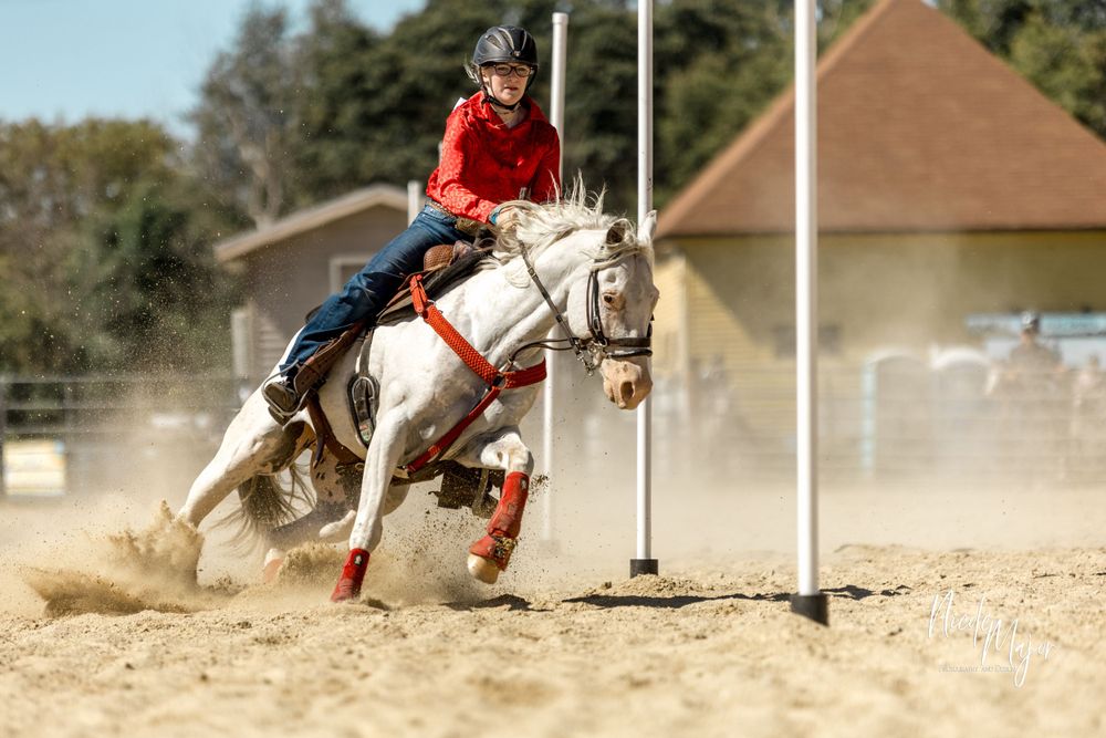 White horse and rider making a sharp turn around a pole in pole bending competition.
