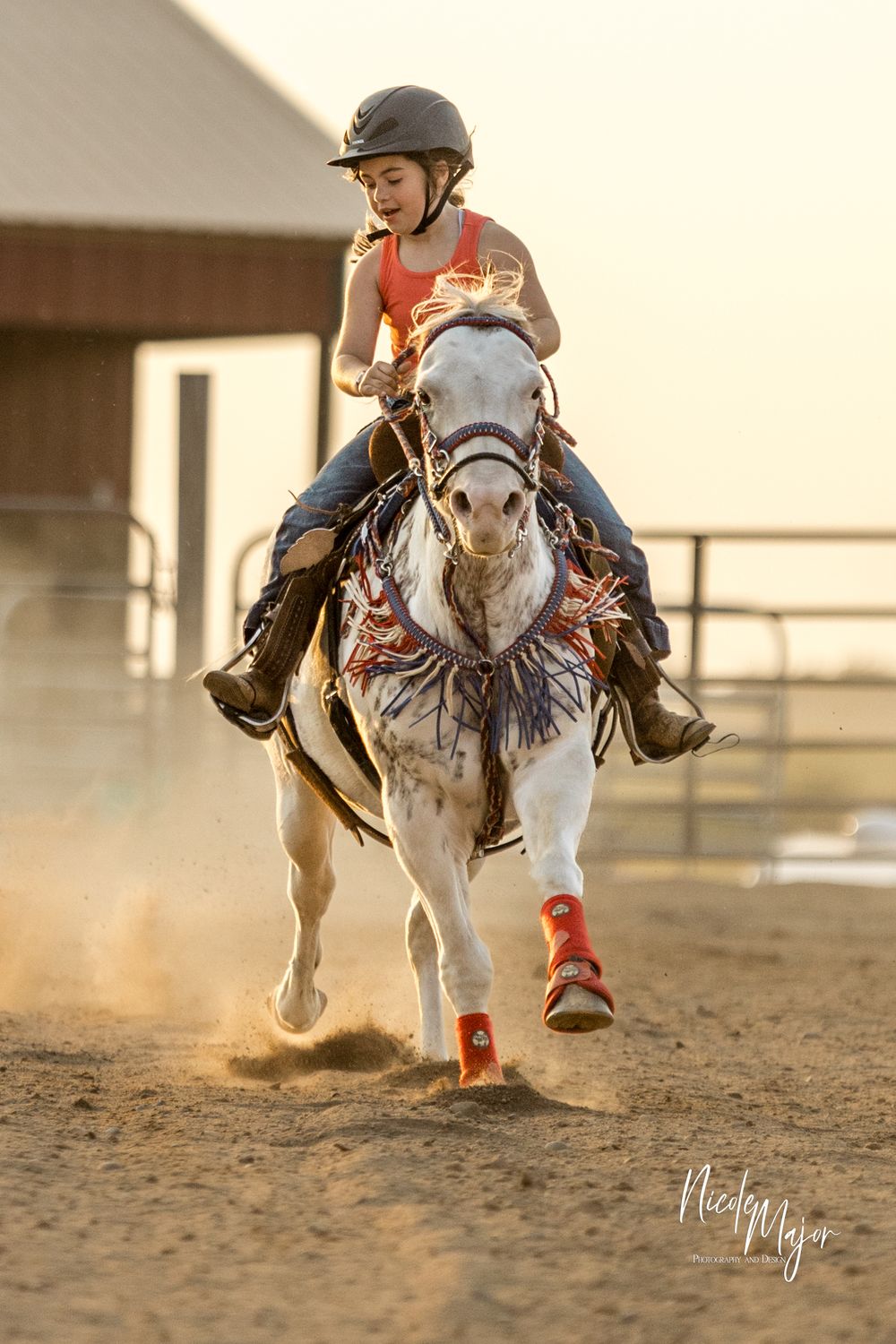 White horse and rider galloping through a dusty arena with red leg wraps during competition.