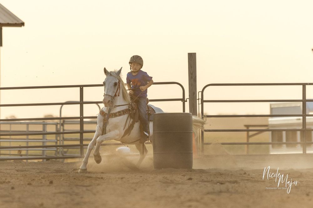 Rider competing in barrel racing on a white horse against a sunset backdrop.