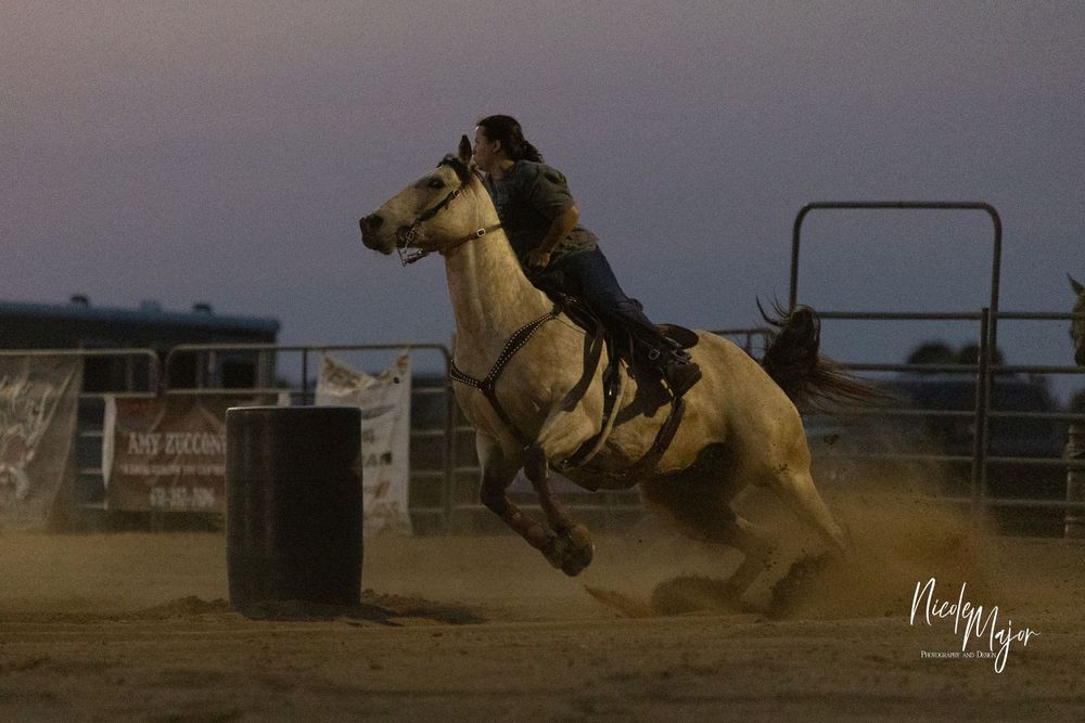 Palomino horse and rider navigating around a barrel in evening competition.