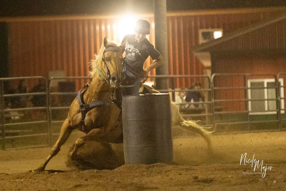 Horse and rider rounding a barrel at night under arena lights during competition.
