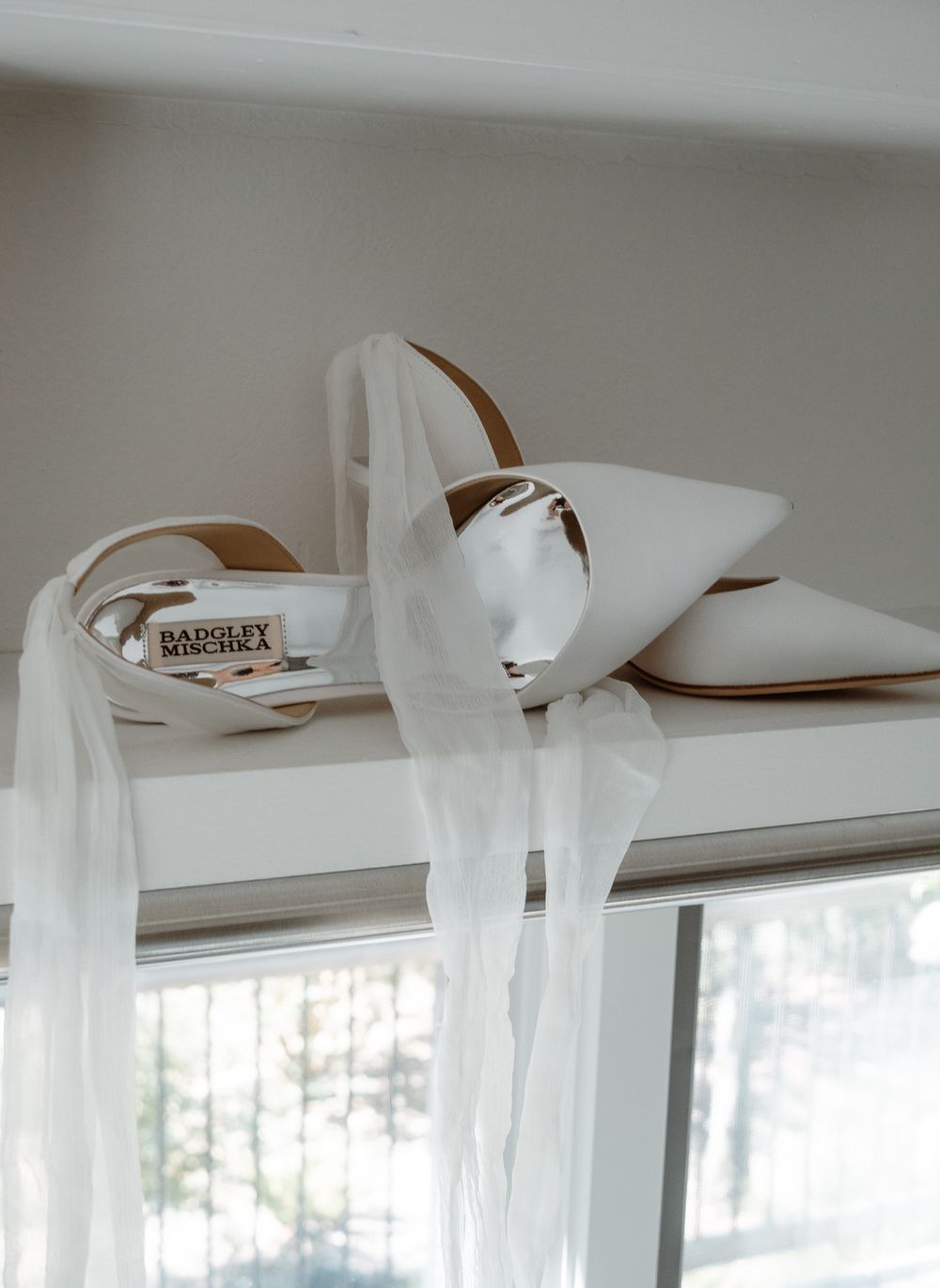 White bridal flats with sheer veil draped over them sit elegantly on a white window ledge.