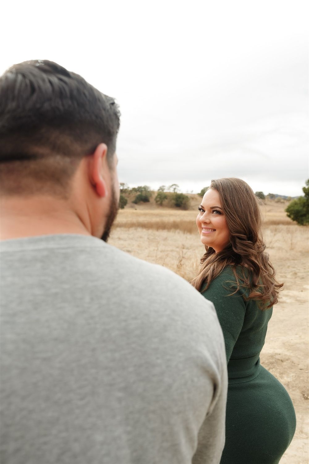A couple shares a romantic moment in an open field on a cloudy day.