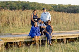 A joyful family of five poses together on a wooden boardwalk surrounded by tall golden grass in Matawan, NJ.