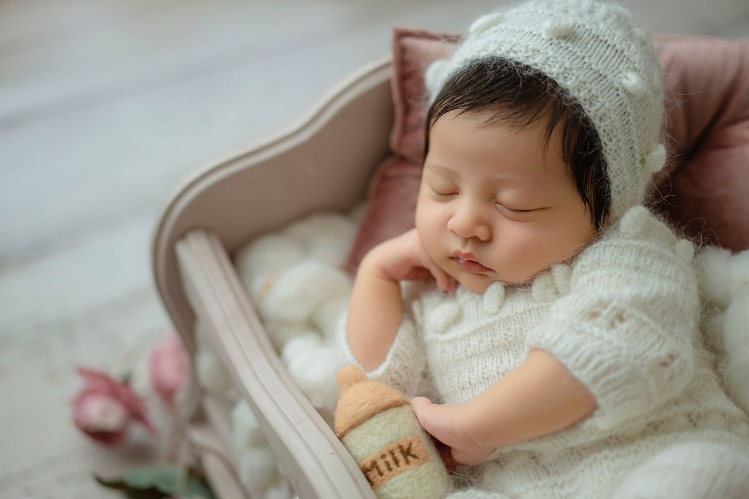 Peaceful sleeping baby in white knit outfit rests in vintage wooden cradle.