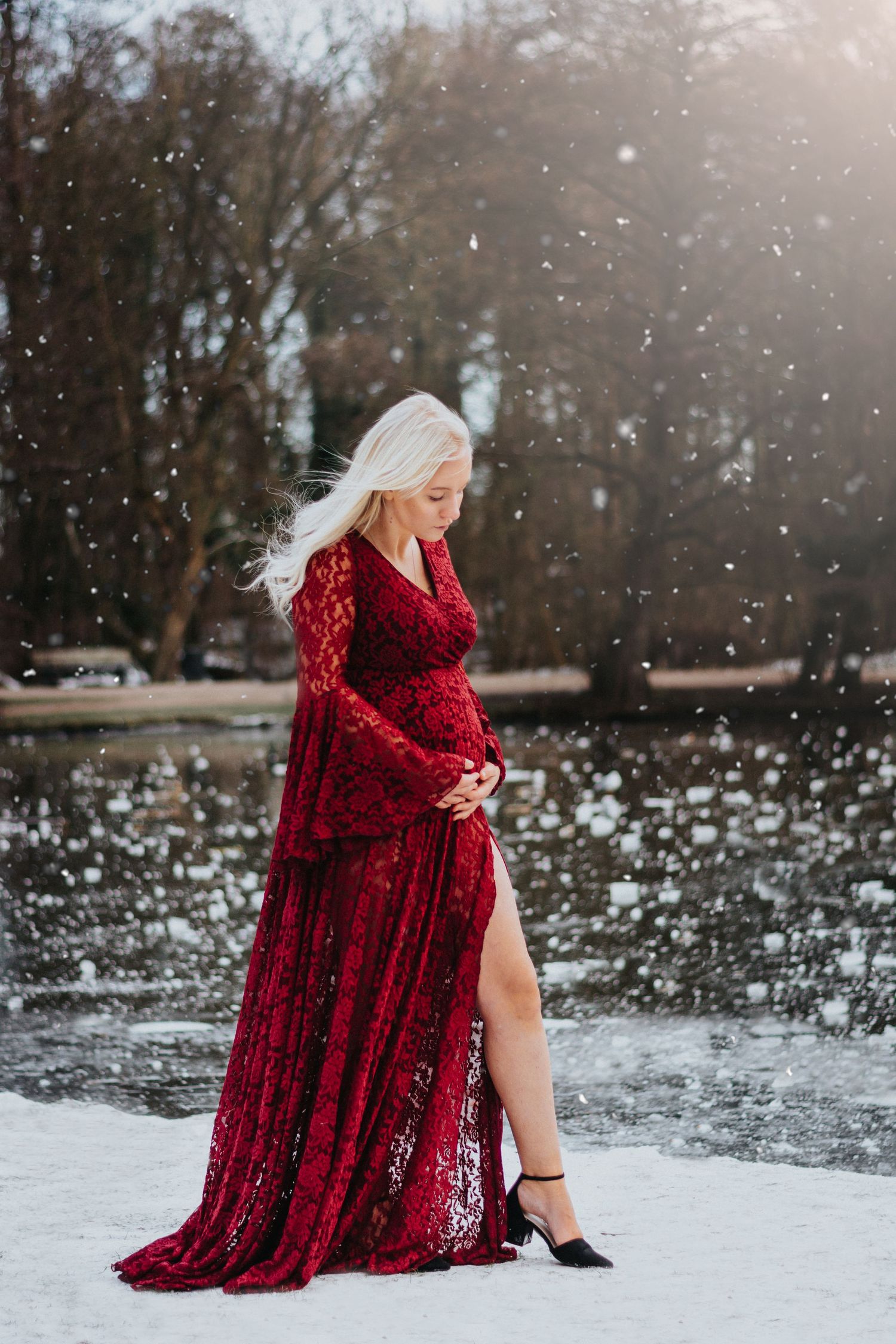 Woman in red lace dress poses in snowy winter scene with falling snowflakes.