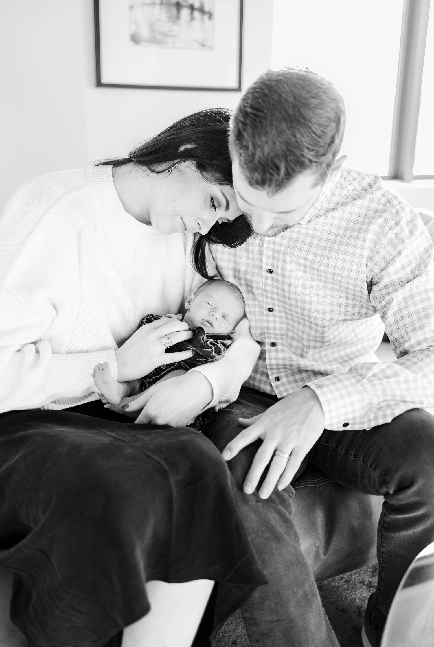 A tender black and white portrait of new parents gazing at their newborn baby.