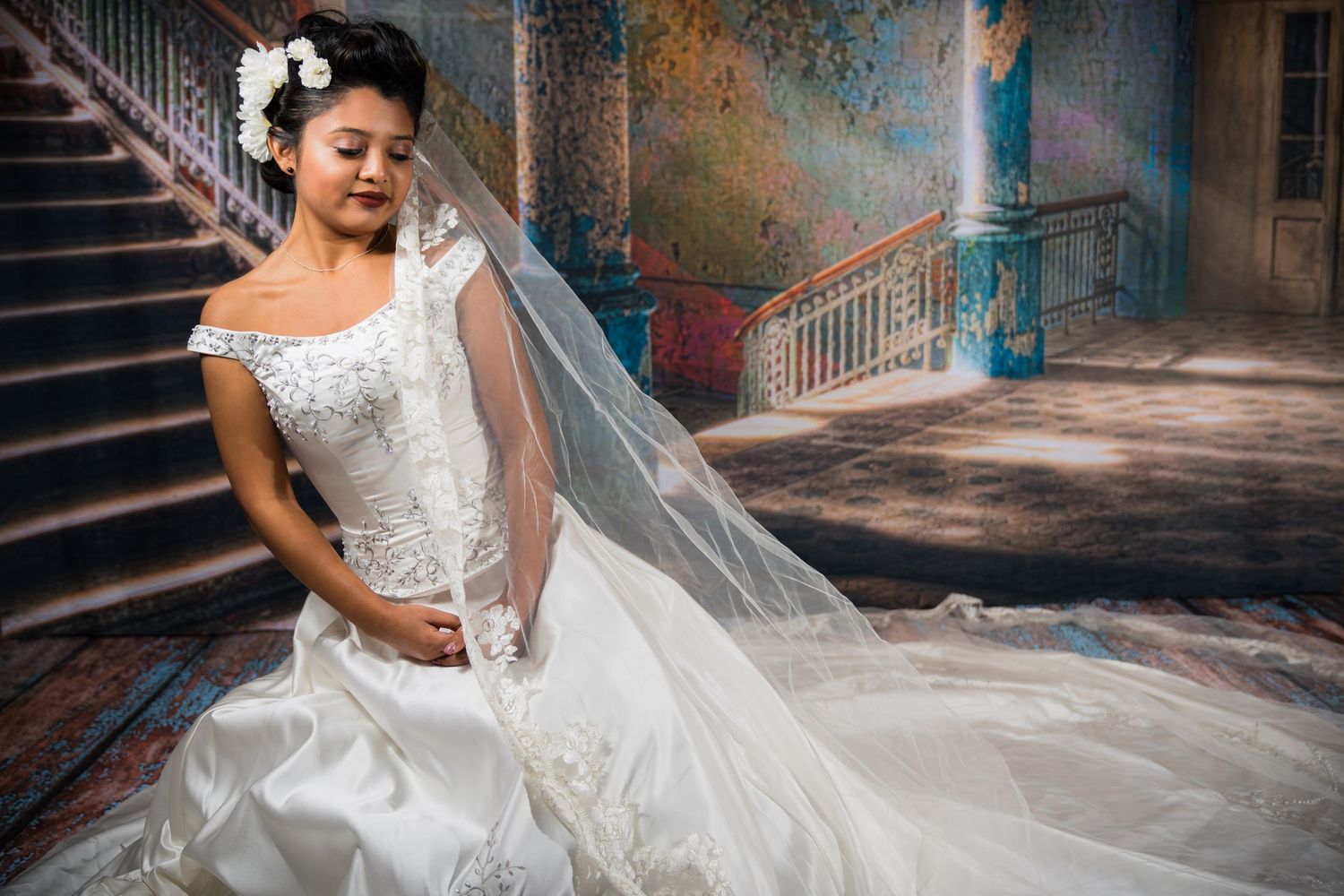 A bride in a white lace wedding dress with long veil poses beside vintage stone stairs in an elegant historic setting.