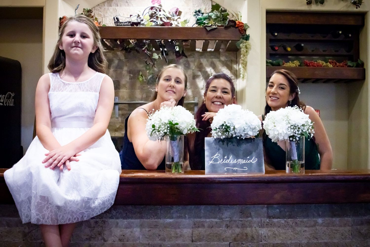 Group seated on wooden ledge at wedding holding white floral bouquets.