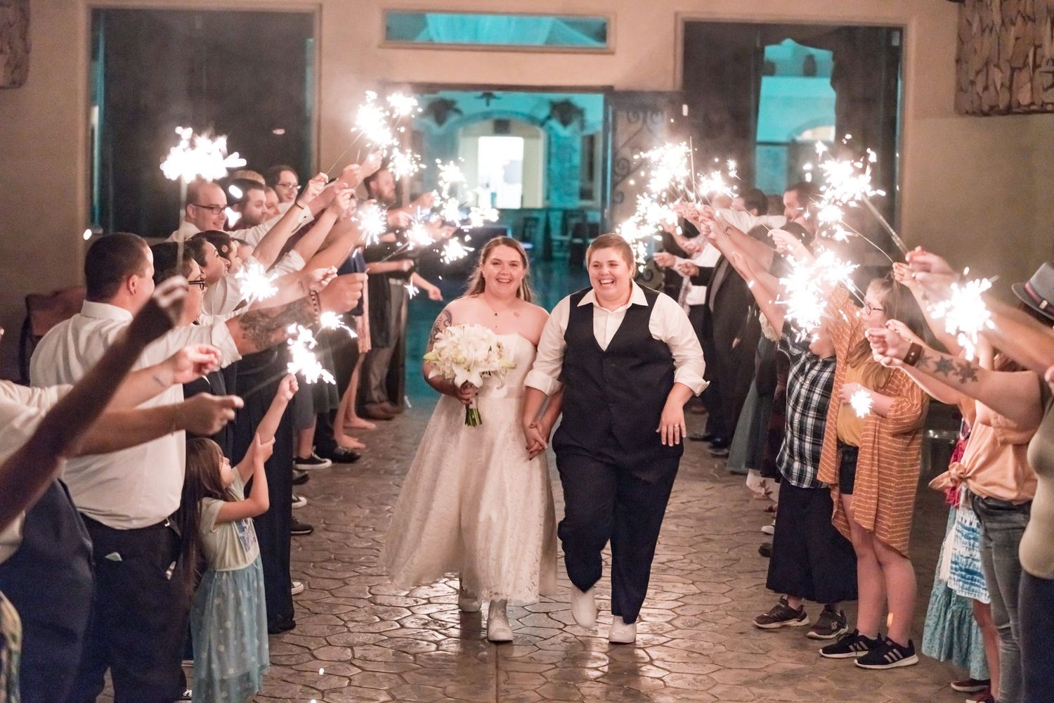 Wedding couple walks through sparkler send-off line during nighttime reception celebration.