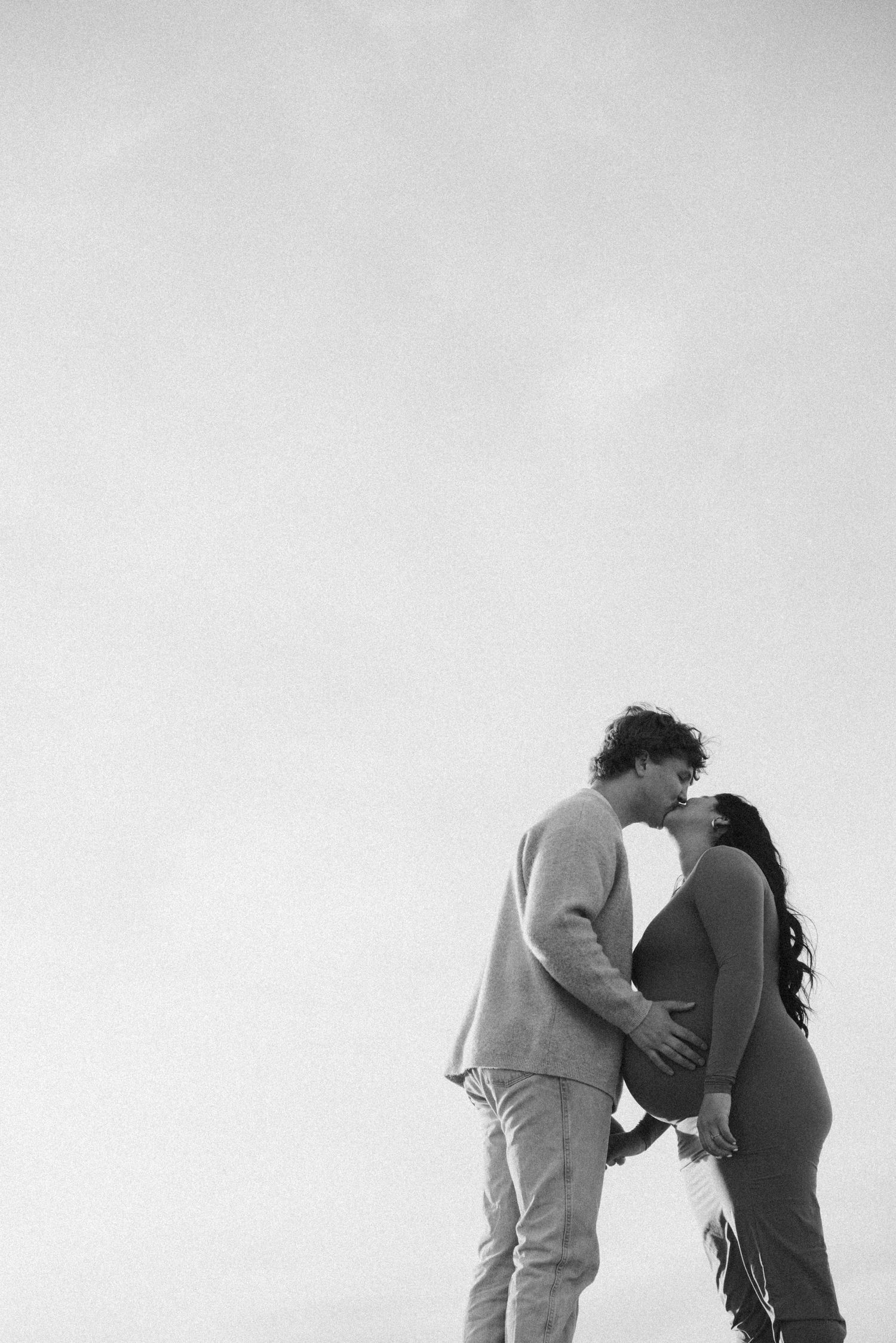 A silhouetted couple shares an intimate moment against a bright sky background.