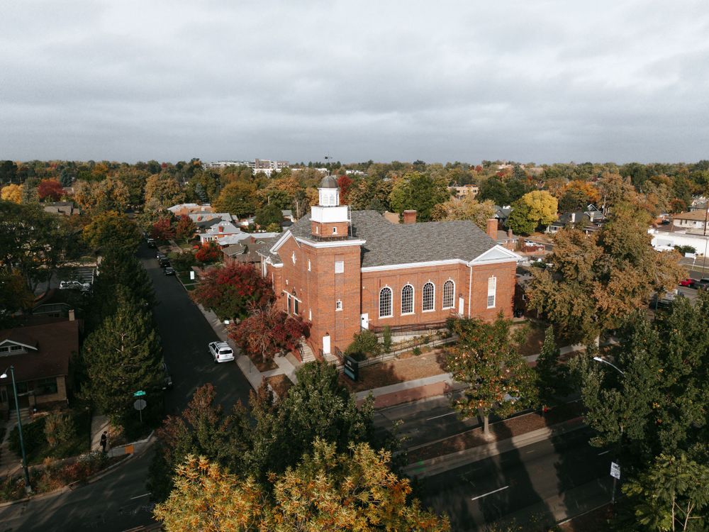 Aerial view of a red brick church surrounded by fall foliage in a suburban neighborhood.