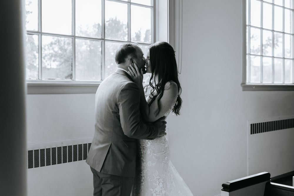 An intimate black and white wedding moment captured by a window.